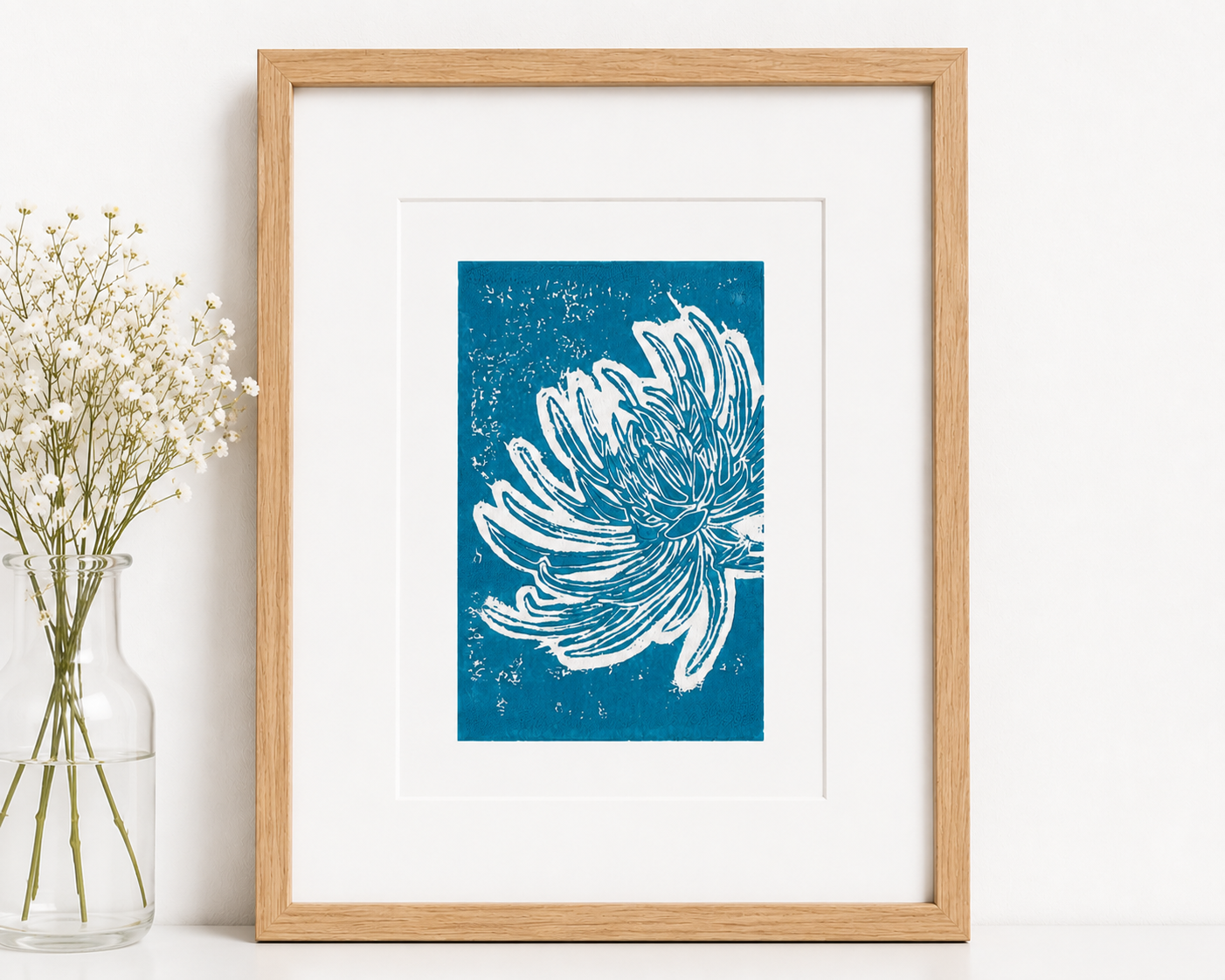 Hand-printed turquoise chrysanthemum linocut on A4 paper displayed in a light oak frame with a white mount in a bright Scandinavian interior