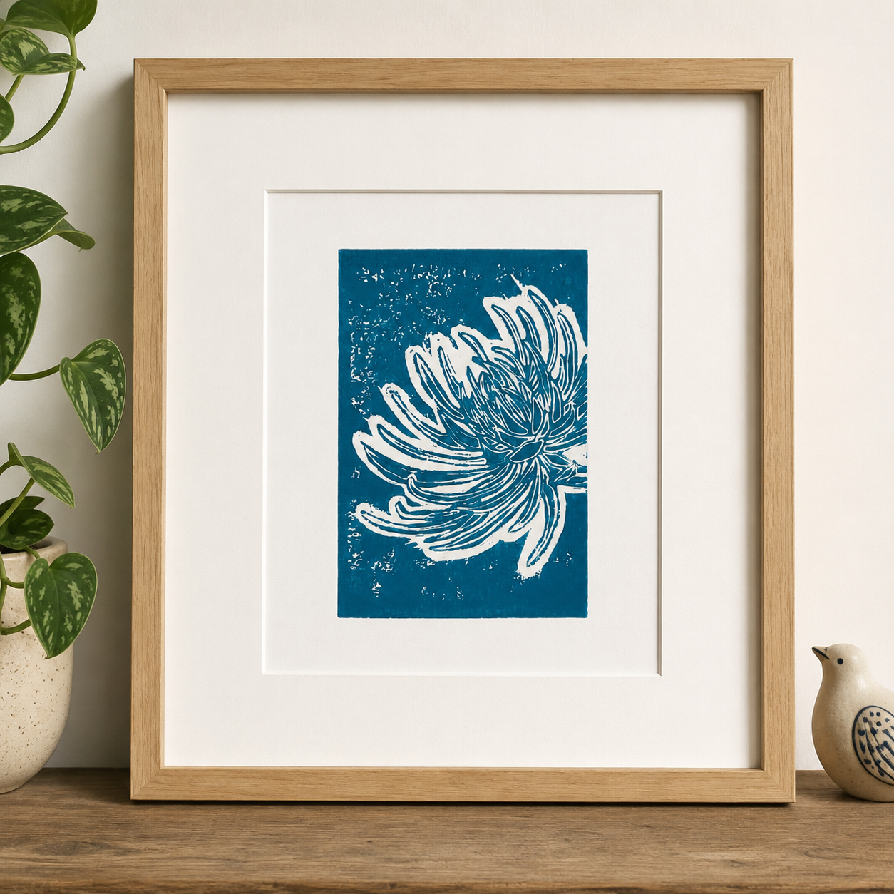 Framed linocut print of chrysanthemum flower on a shelf with a small bird and plants