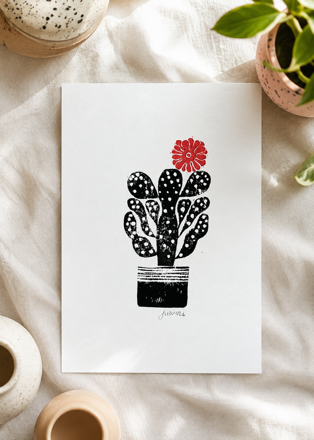 handmade linocut print of a cactus with a flower in black and red ink, A4 size, signed artwork, overhead product shot