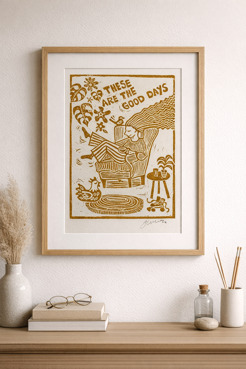 Framed artwork with 'These are the good days' text on a wall above a wooden shelf.