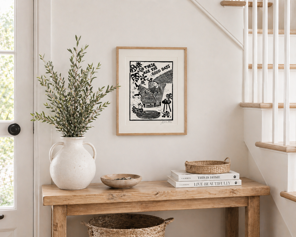 Nook with a wooden table, vase with greenery, framed artwork, and books.