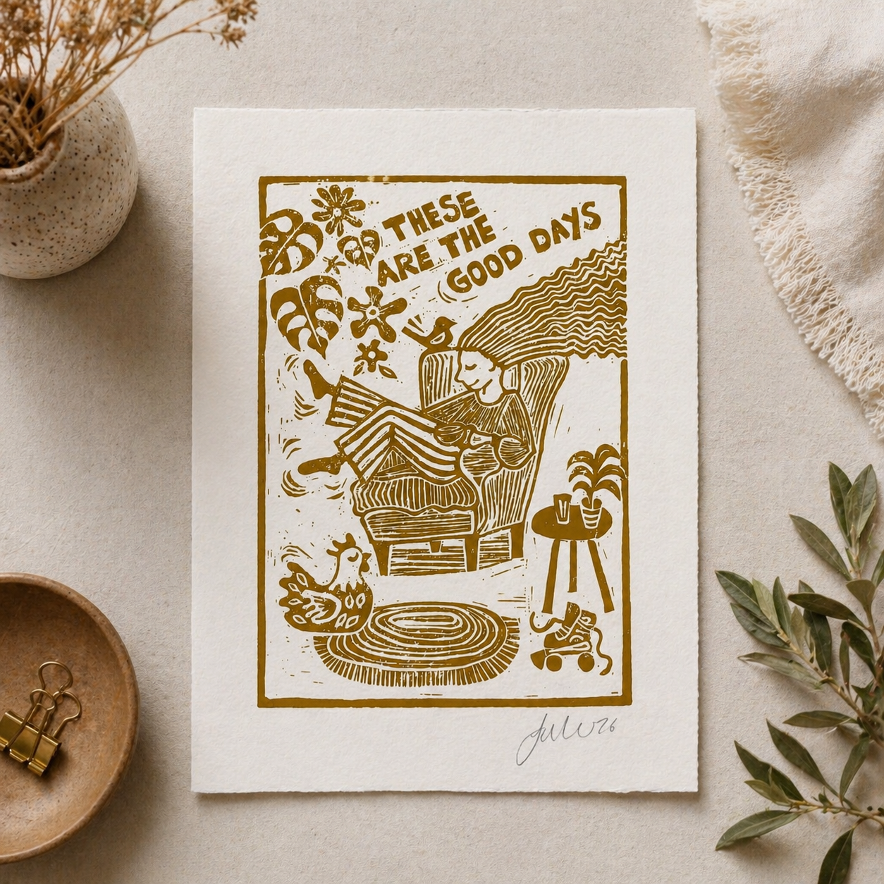 Poster with a gold illustration of a person sitting in a chair with text 'These are the good days' on a beige surface.