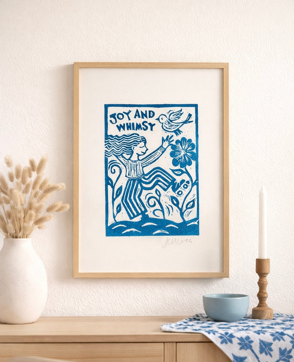 Framed artwork with a blue design of a woman and birds on a white wall.