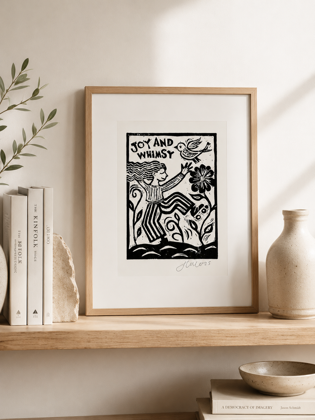 Framed artwork with 'Joy and Whimsy' text on a shelf with books and decor.