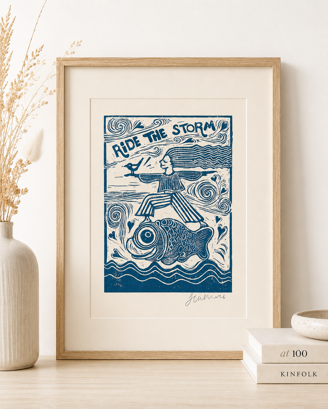 Framed artwork with a blue and white design of a person riding a fish, titled 'Ride the Storm', on a neutral background.