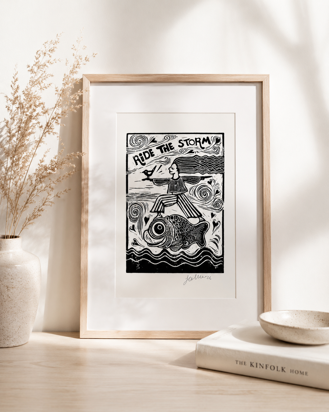 Framed black and white artwork titled 'Ride the Storm' on a light wooden surface with decor items.