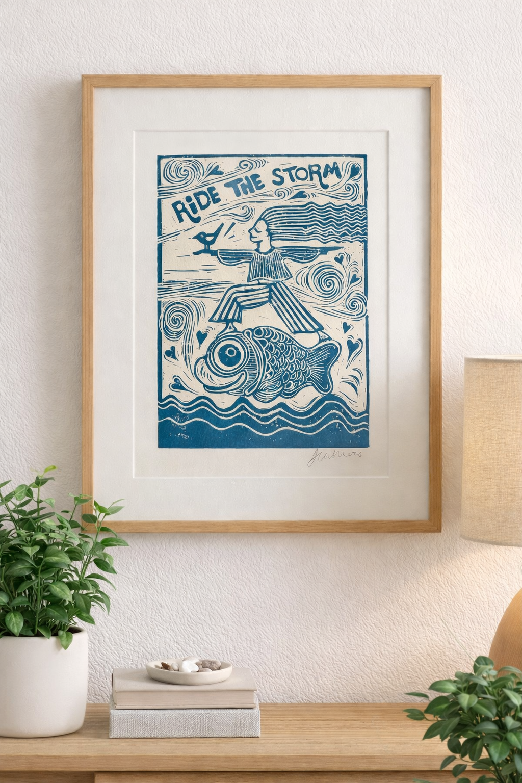 Framed artwork with a design of a person riding a wave titled 'Ride the Storm' on a wall above a wooden shelf.